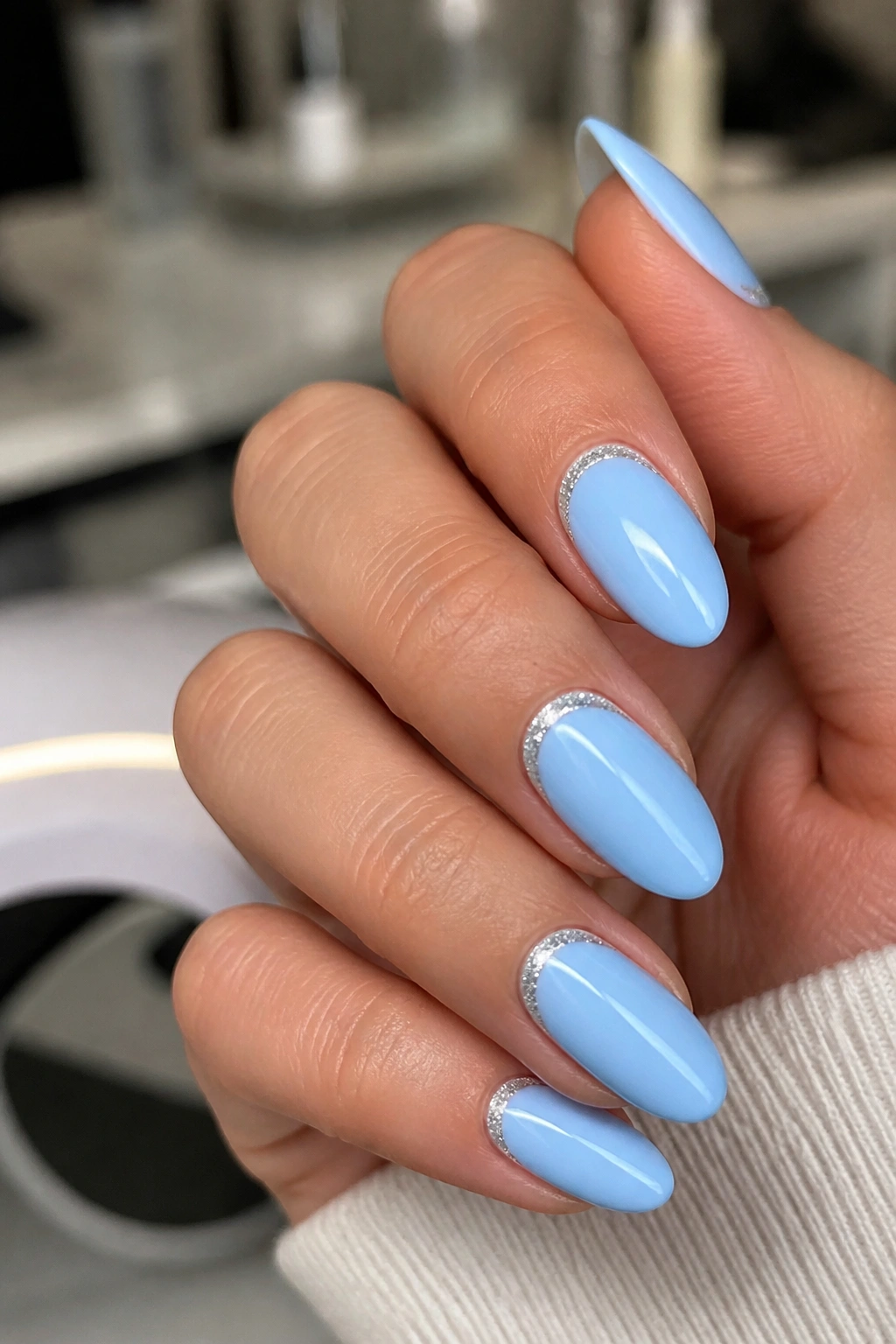 Close-up of almond nails with a fine silver glitter line at the cuticle on a blue base