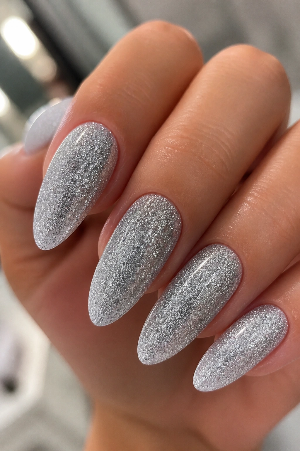 Close-up of almond nails fully covered in fine silver glitter