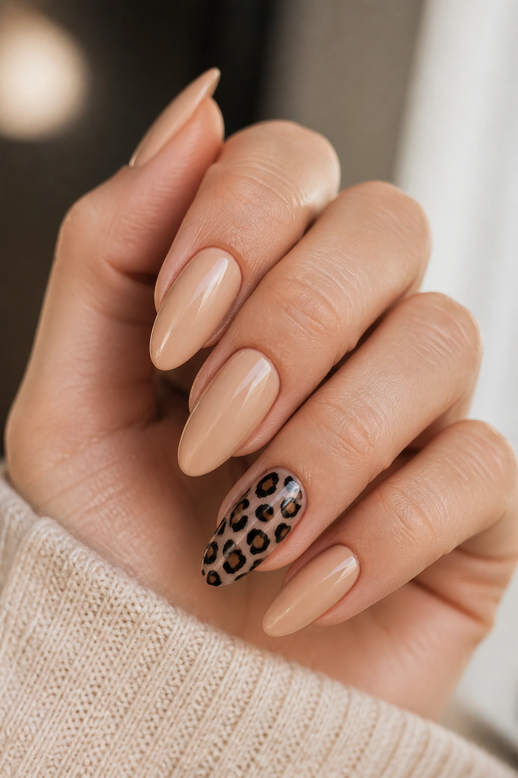 Hand with one accent cheetah nail among nude almond nails