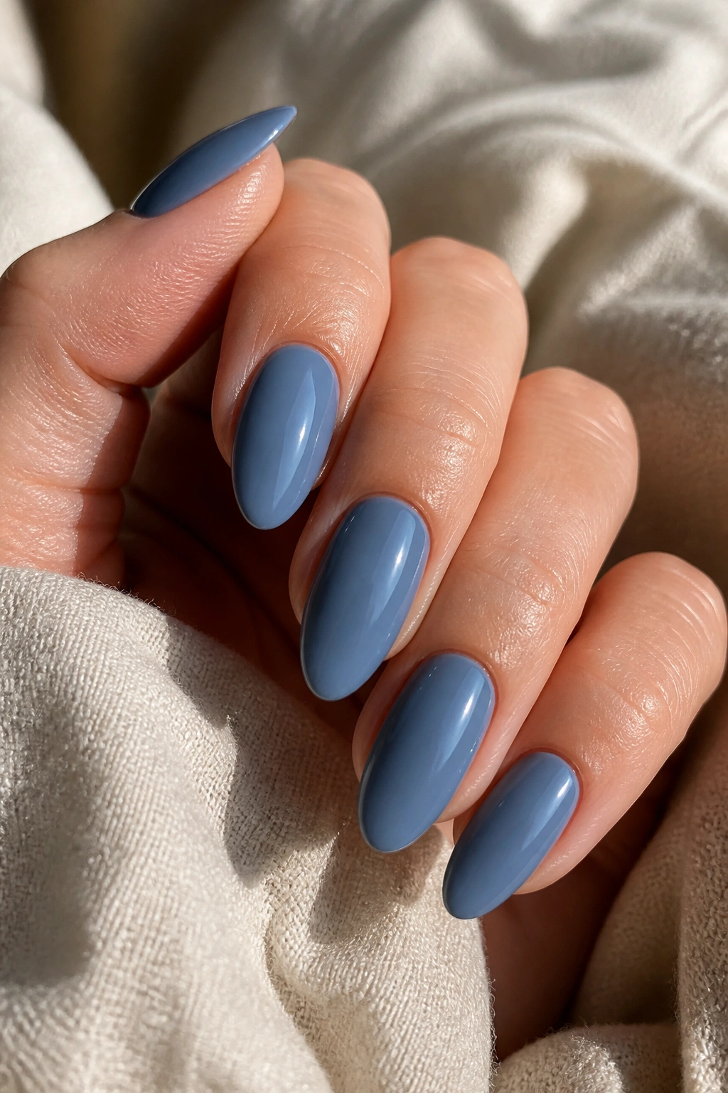 Close-up of slate-blue almond nails on a real hand with glossy finish