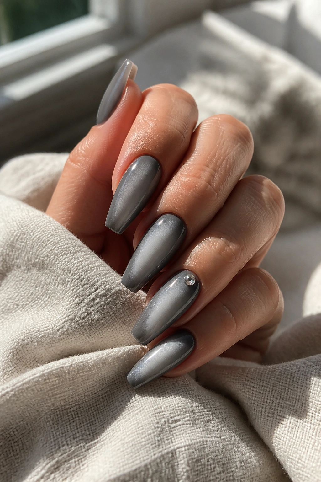 Close-up of coffin nails with smoky base and soft silver aura on real hand under natural window light