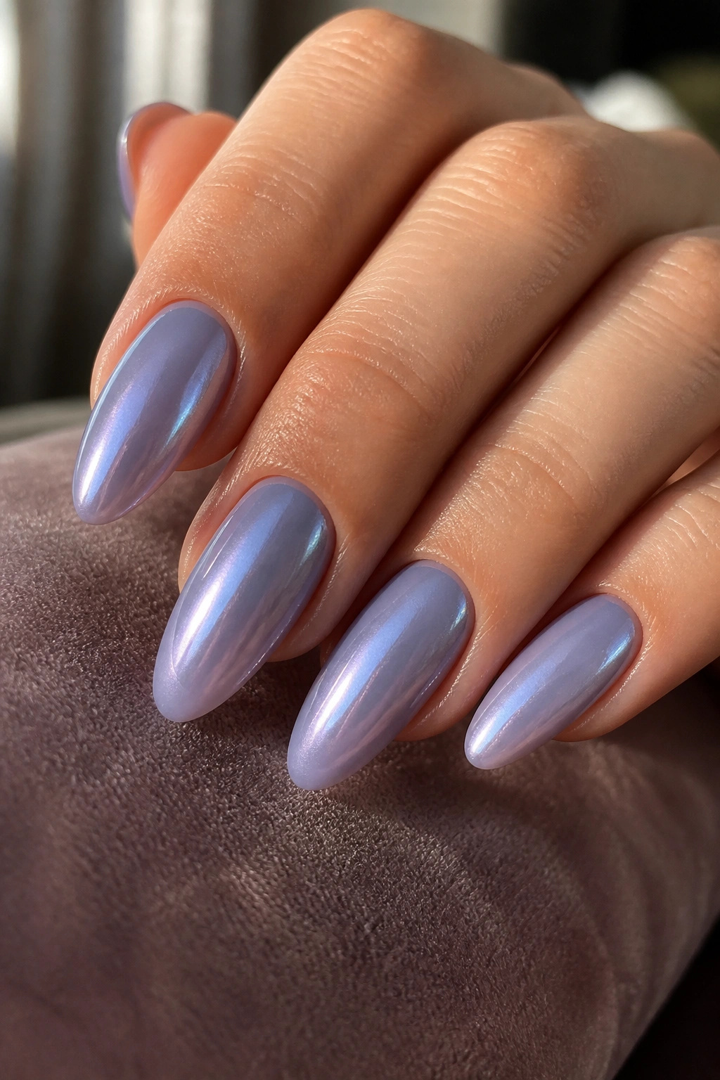Close-up smoky lavender almond nails with pearl finish on a hand, warm glow
