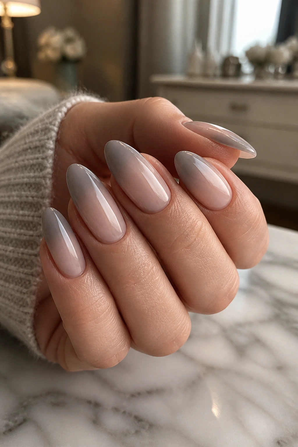 Close-up of smoky nude almond nails with gray ombre on a real hand, soft window light