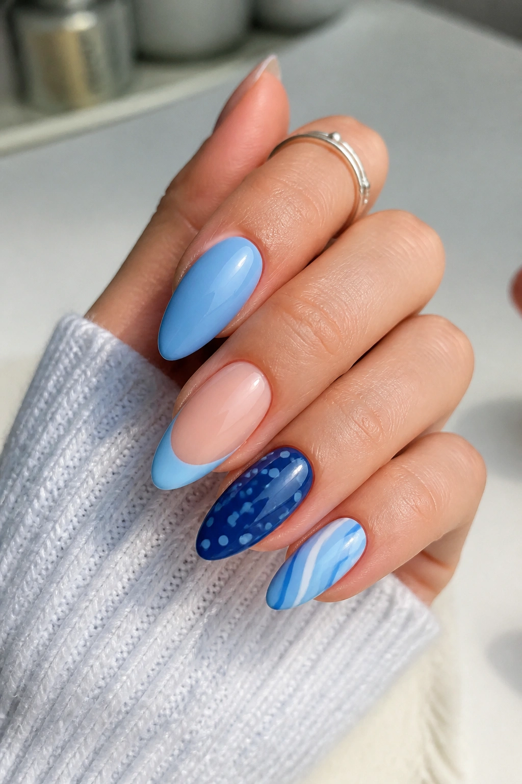 Close-up of a hand with almond nails in coordinated soft blue tones showing different finishes