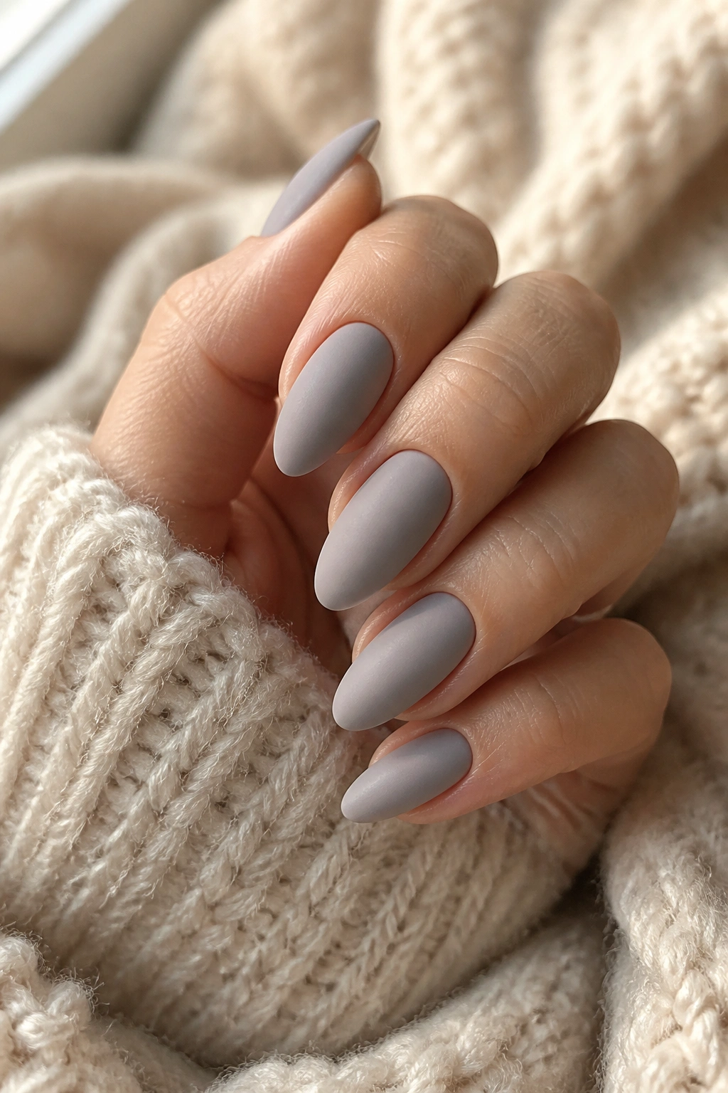 Close-up of a hand with soft gray cashmere velvet almond nails on a knit blanket