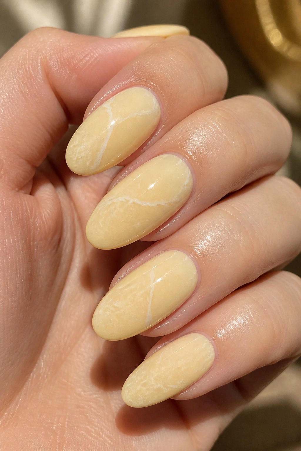 Almond nails with pale yellow base and thin white veins for a soft marble look.