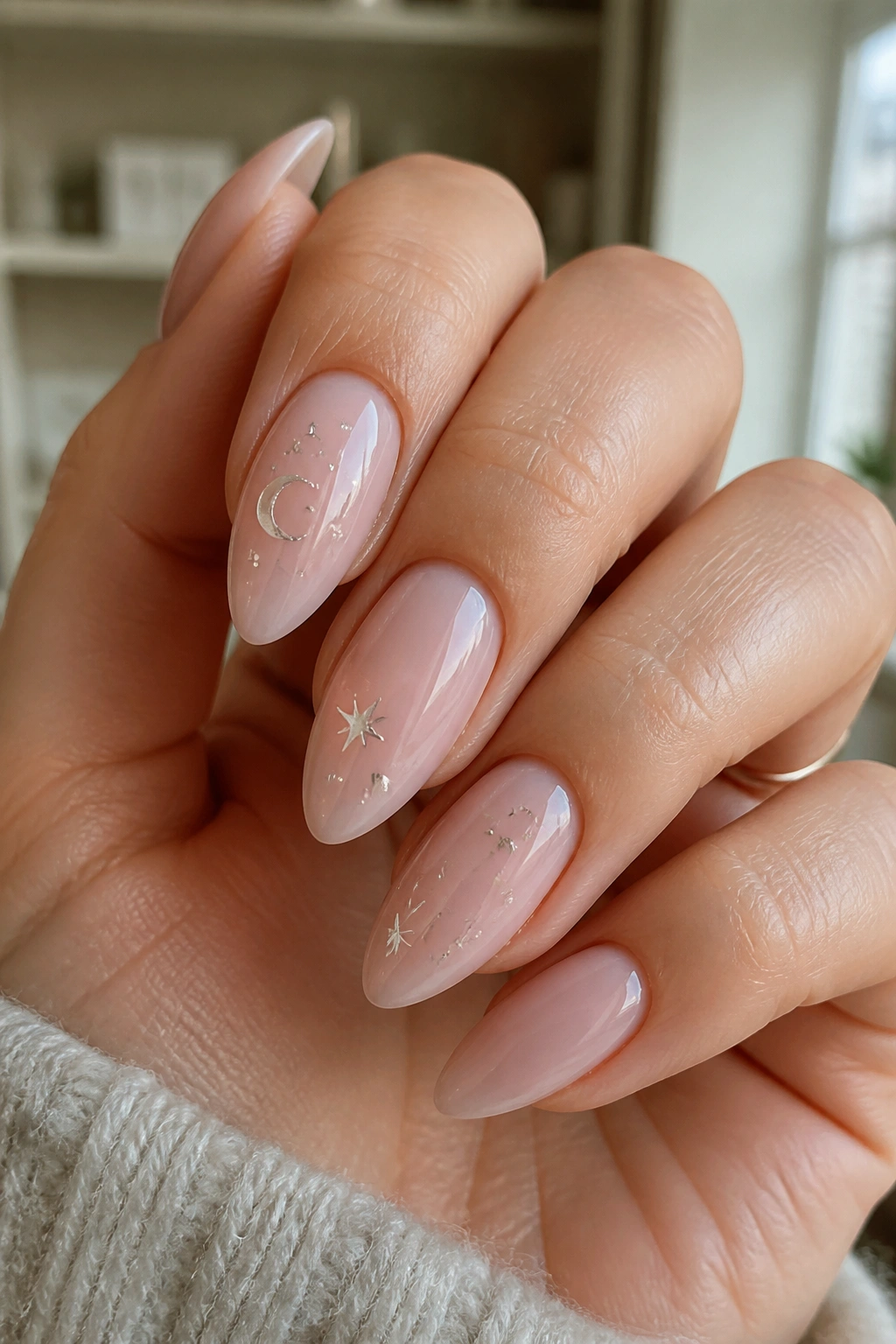 Close-up of almond nails with tiny silver stars and a crescent moon