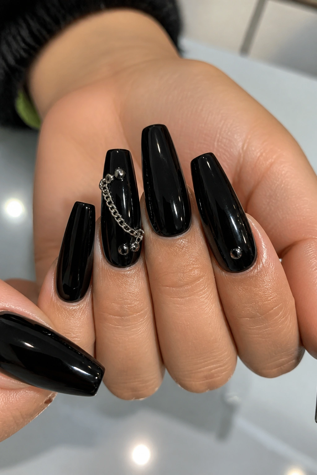 Close-up of black coffin nails with tiny studs and a chain on real hand