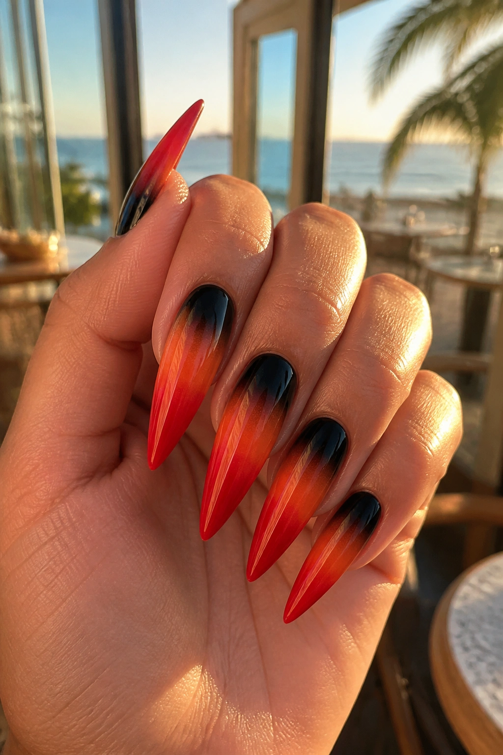Close-up of hand with black-to-orange-to-red ombre nails.