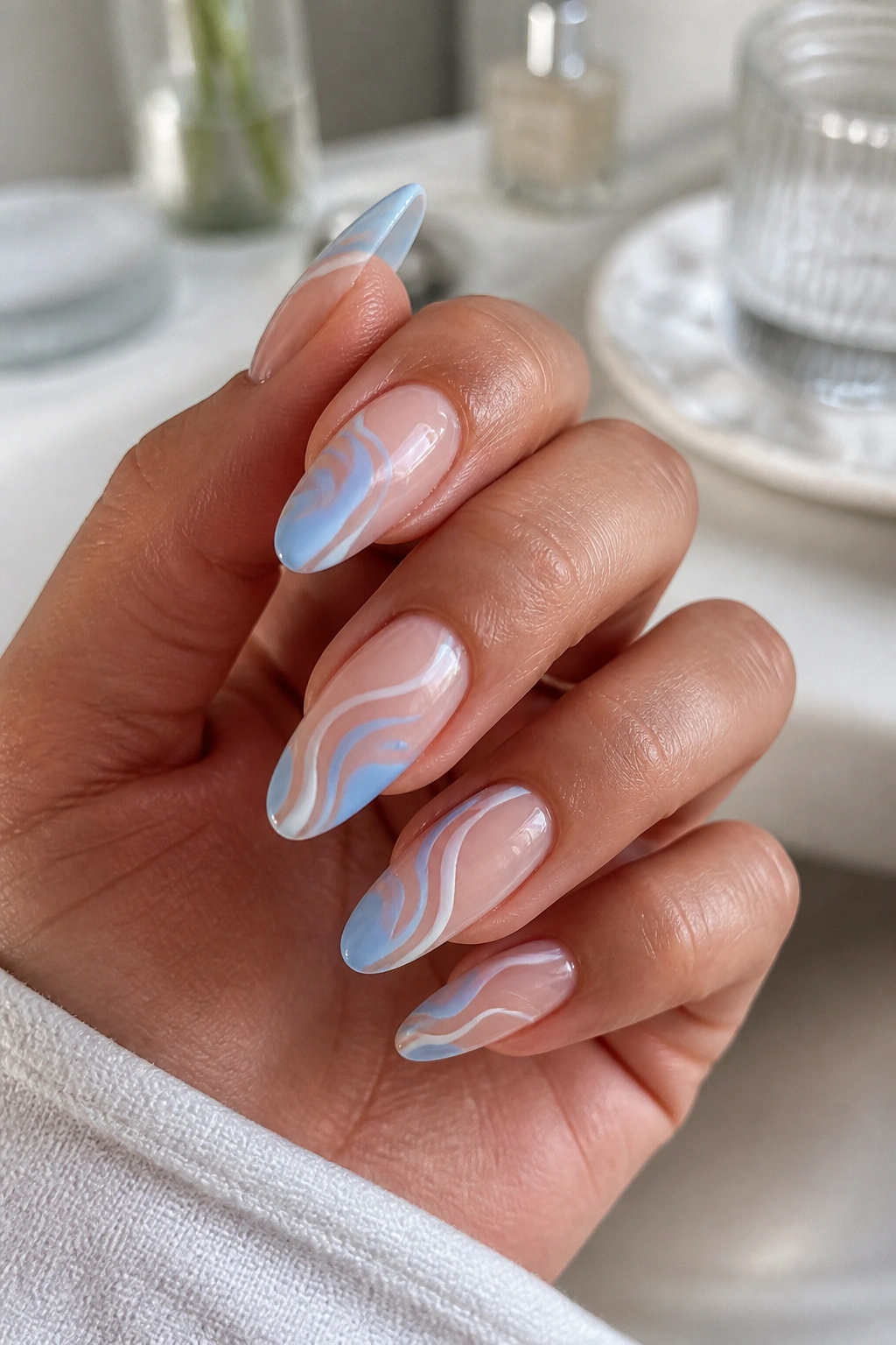 Close-up of almond nails with blue abstract swirls on a nude base