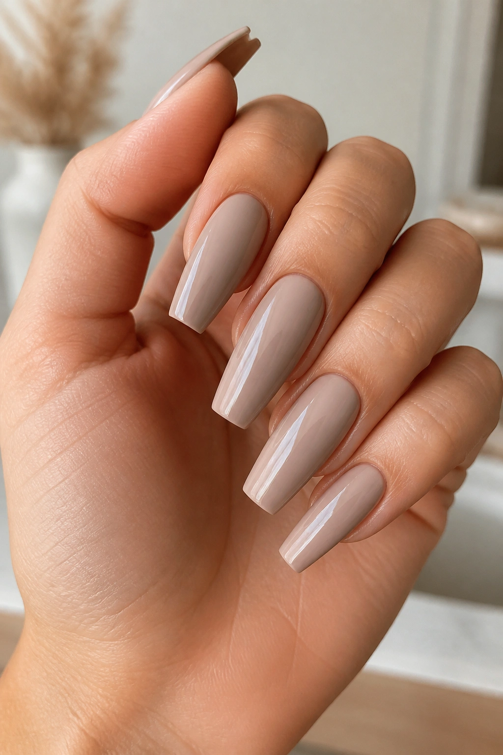 Close-up of soft taupe nude coffin nails on a real hand in a salon setting