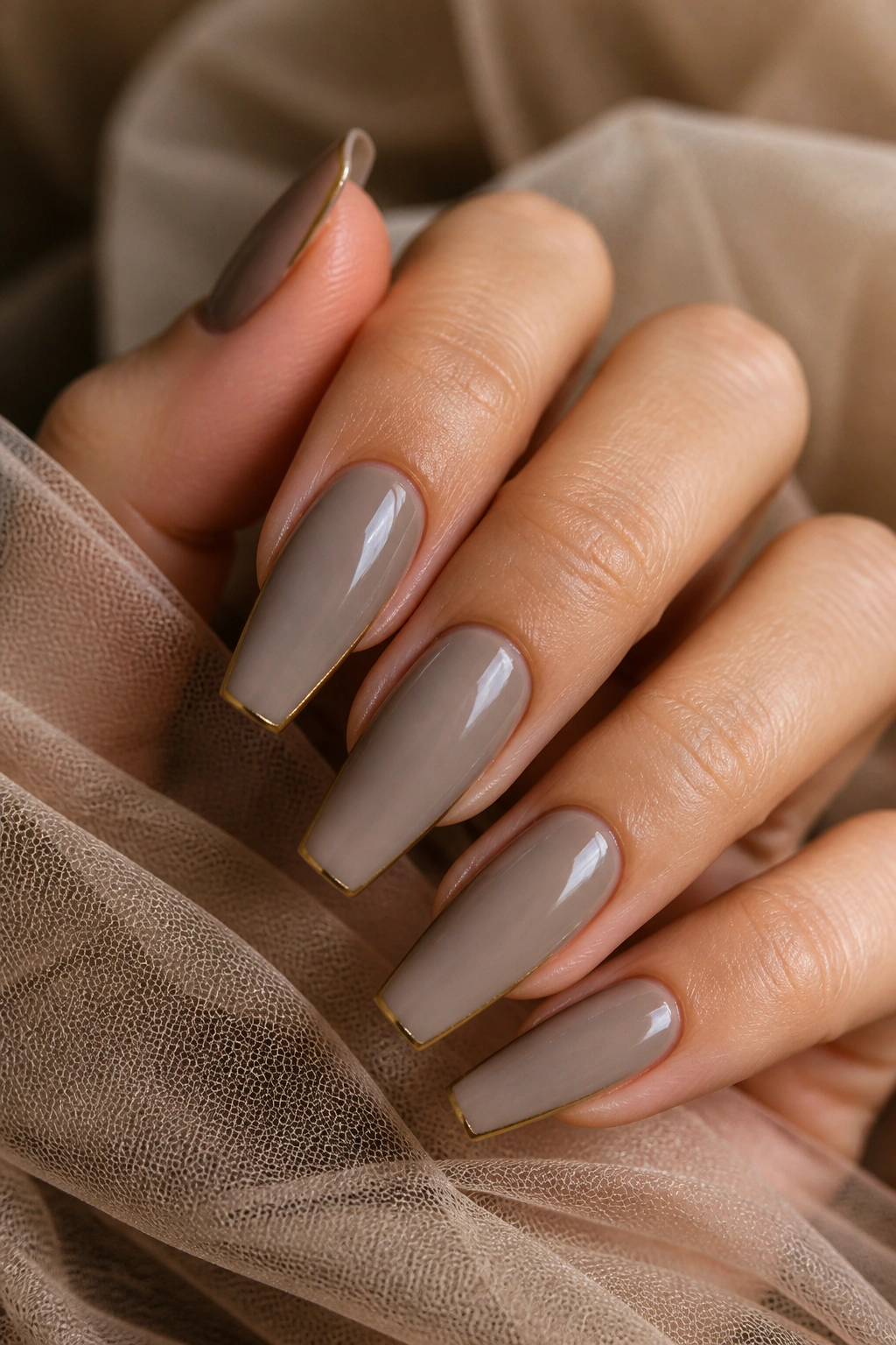 Close-up of taupe coffin nails with fine gold outline on a real hand