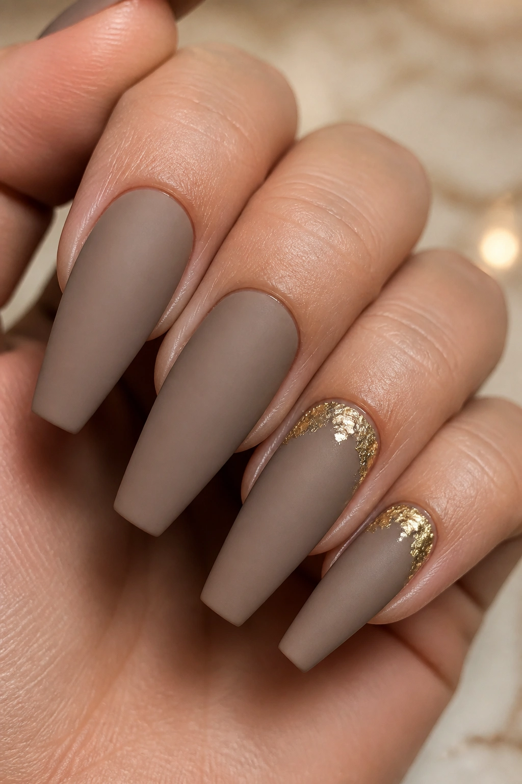 Close-up of taupe matte coffin nails with gold foil at the cuticle