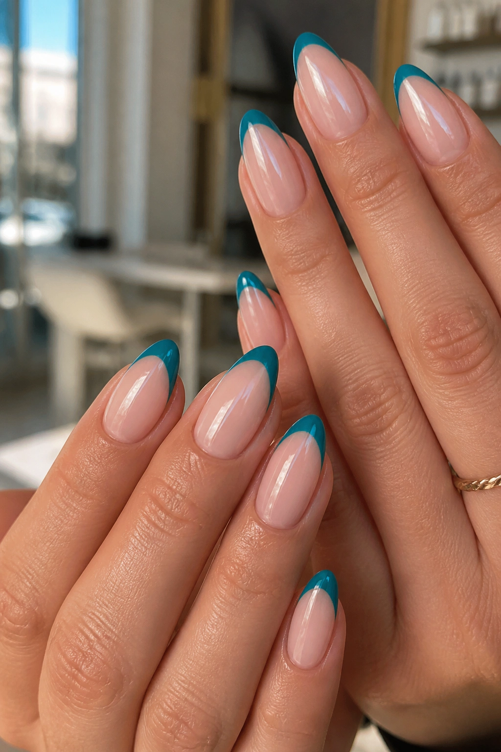 Close-up of almond nails with teal French tips on a nude base