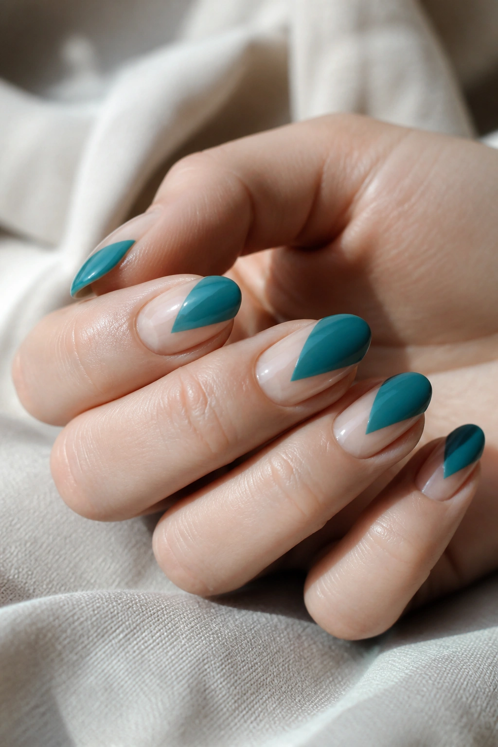 Close-up of teal color-block almond nails showing negative-space diagonal block on a real hand