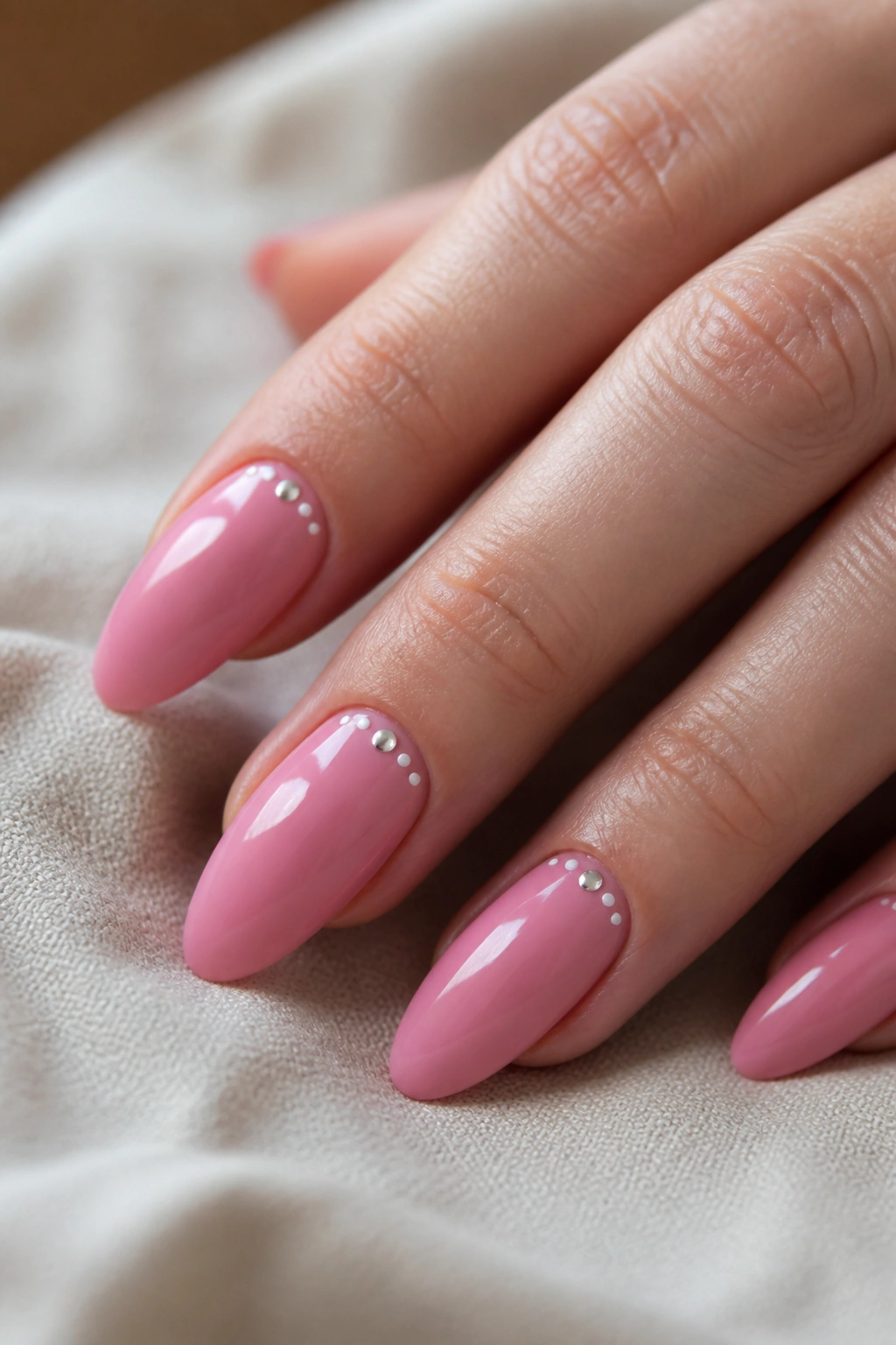 Close-up of almond nails with tiny dot accents near the cuticle on a pink manicure