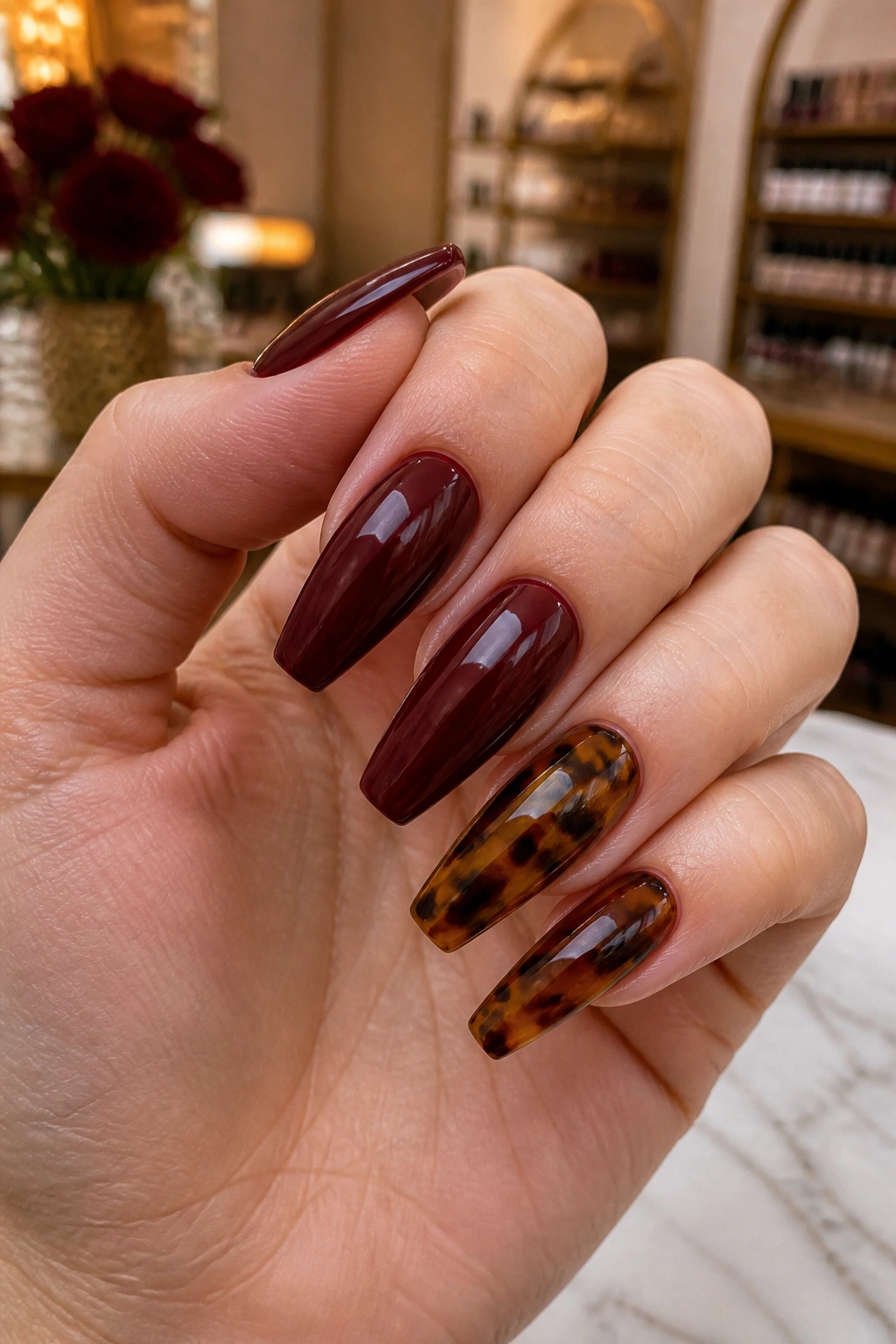 Close-up of burgundy coffin nails with tortoiseshell accents on a real hand