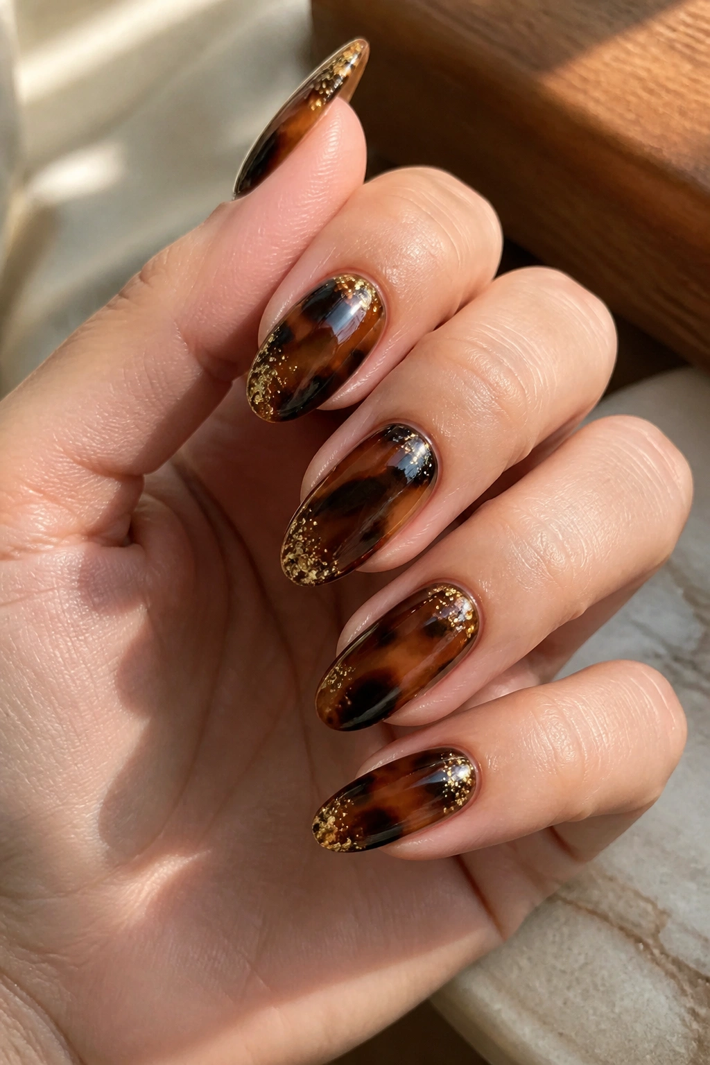 Almond nails with tortoiseshell pattern and gold glitter accents