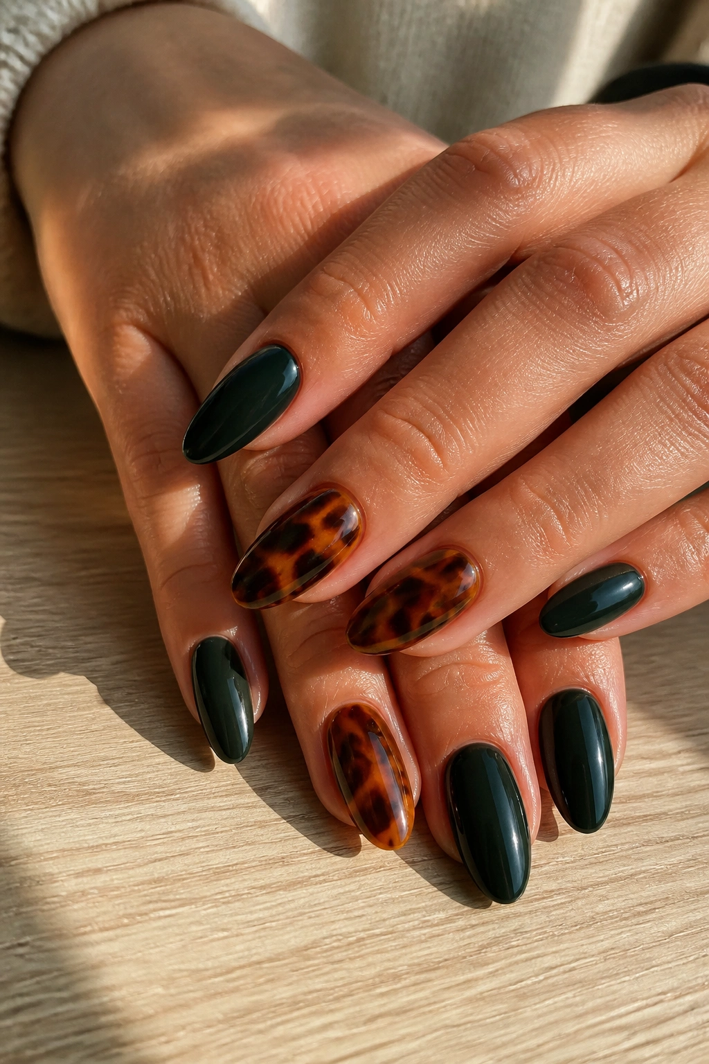 Close-up of tortoiseshell and dark green almond nails on real hands