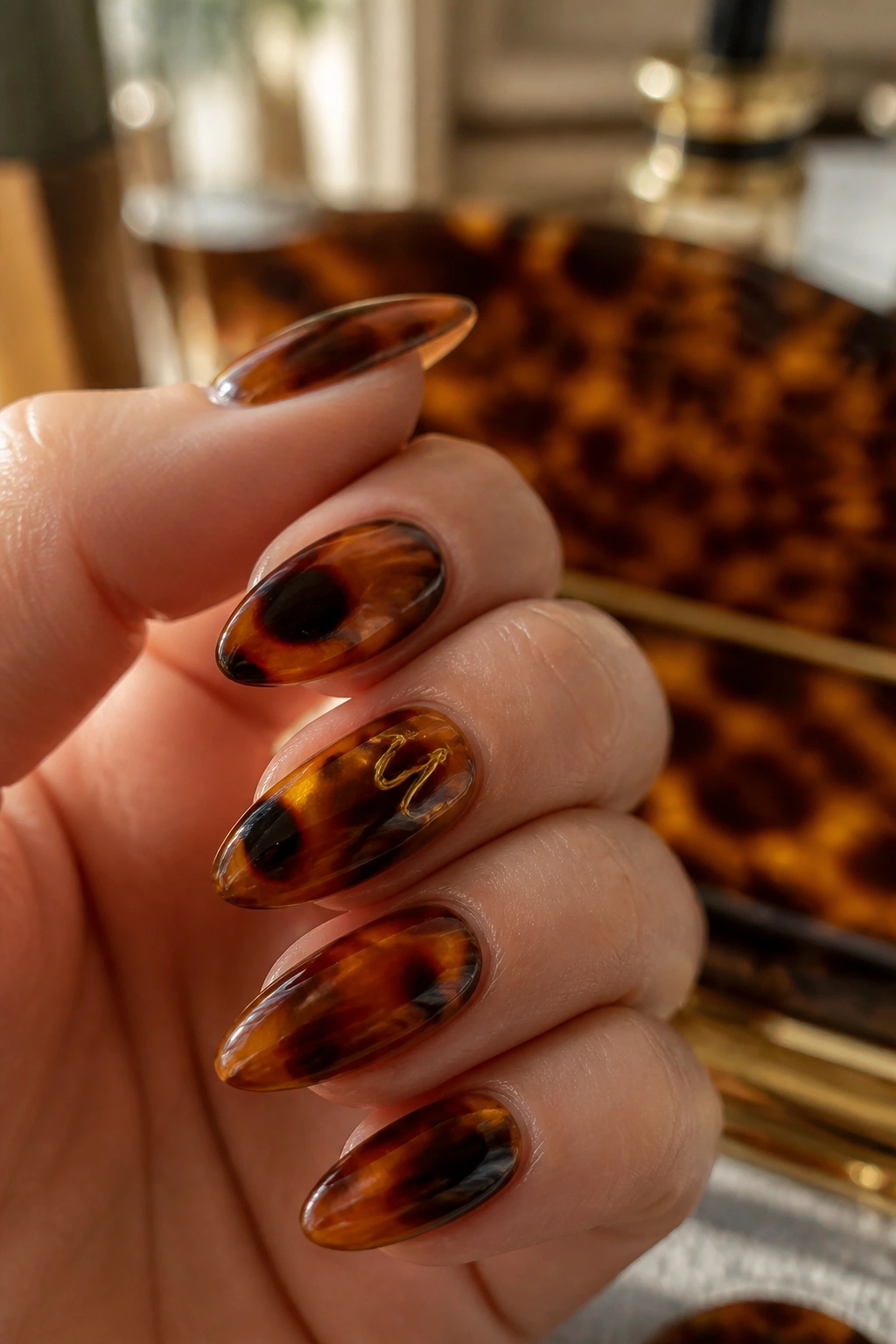 Close-up almond nails with tortoiseshell pattern and abstract initial motif