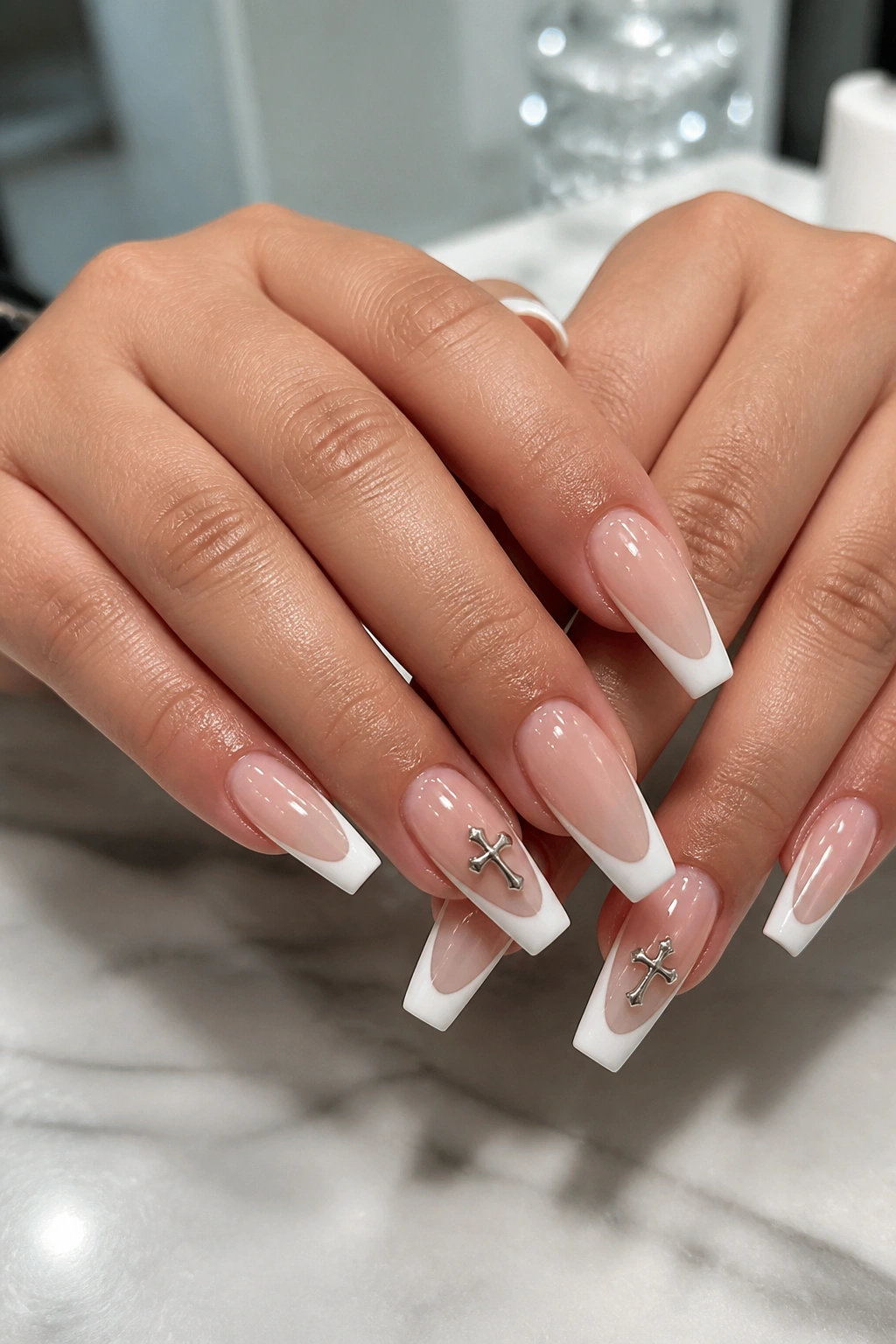 Close-up of hands with white French tip coffin nails and tiny cross charms on accent nails.