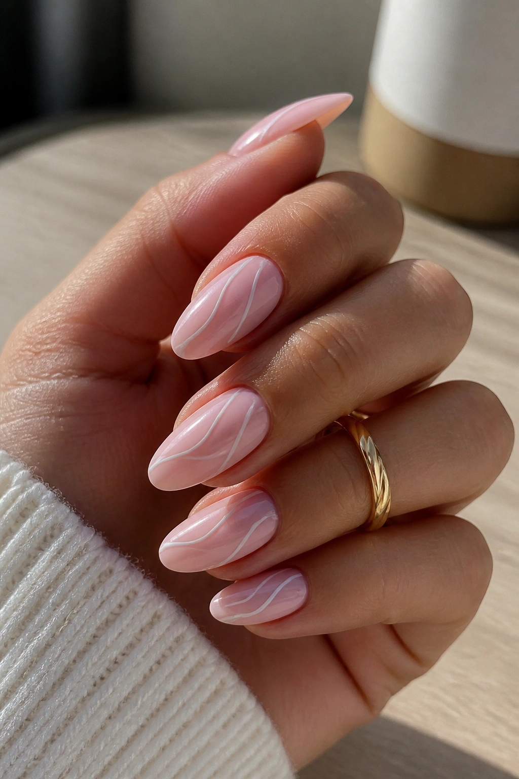 Close-up of a real hand with almond nails and white swirl designs on light pink