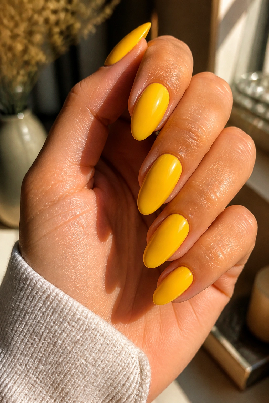 Close-up of almond nails painted solid yellow with a soft gloss on a real hand