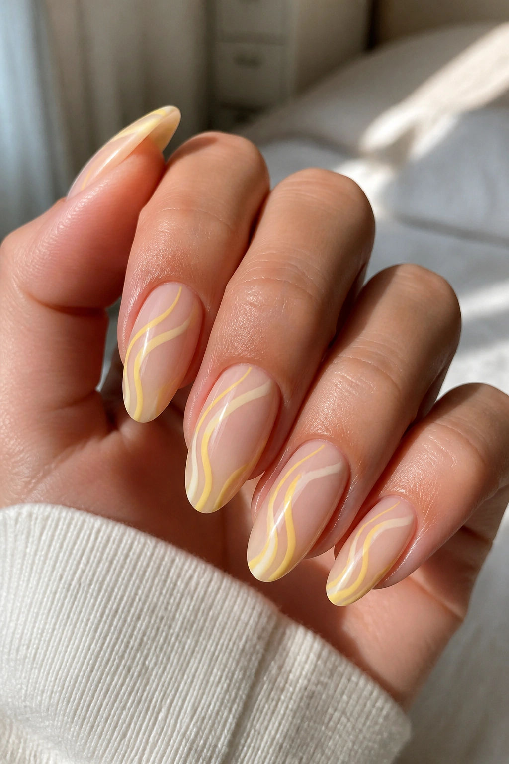Close-up of almond nails with butter-yellow swirls on a sheer base.